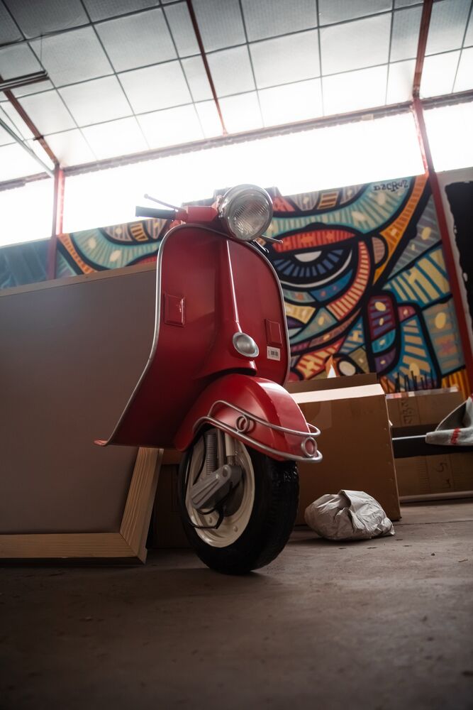 Scooter Vespa rouge devant un mur de graffitis